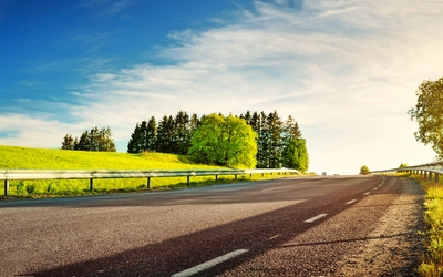 Straße durch eine grüne Landschaft mit Bäumen und einem blauen Himmel im Sonnenlicht