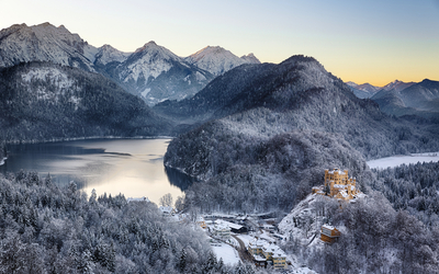 Winterliche Berglandschaft mit Schloss und See bei Sonnenuntergang.