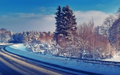 Verschneite Straße durch eine winterliche Landschaft bei Sonnenuntergang.