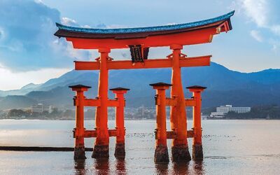 Japanisches Torii-Tor im Wasser vor einer Gebirgskulisse bei Sonnenuntergang.