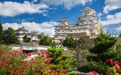 Japanische Burg umgeben von Gärten und blauem Himmel.