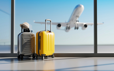 Zwei Koffer am Flughafenfenster mit startendem Flugzeug im Hintergrund.