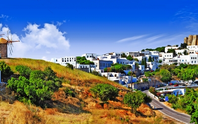 Windmühlen und eine Burg auf einem Hügel über einer weißen Siedlung bei klarem Himmel