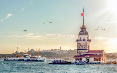 Leuchtturm im Meer bei Sonnenschein, mit vorbeifahrendem Schiff und Vögeln am Himmel.