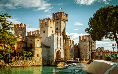 Burg am Wasser mit Booten und italienischer Flagge oben.